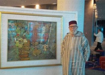 El pintor Pepe Gámez posa junto a una de sus obras, llevando una chilaba y un fez.