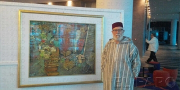 El pintor Pepe Gámez posa junto a una de sus obras, llevando una chilaba y un fez.