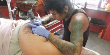 Pancho en su estudio, tatuando un mándala en el muslo de su clienta, Patricia.