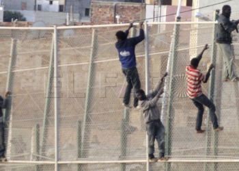 GRA079. MELILLA, 15/10/2014.- En torno a un centenar de inmigrantes permanecen encaramados en la valla fronteriza entre Melilla y Marruecos y se niegan a bajar como les indica la Guardia Civil, que mantiene un despliegue de seguridad en la zona de Villa Pilar, entre el aeropuerto de Melilla y el cementerio musulm·n de Sidi Guariach.Numerosas patrullas de la Guardia Civil han formado un cordÛn de vehÌculos a pie de valla en un tramo amplio del perÌmetro, donde los subsaharianos permanecen desde pasadas las 06:30 horas, cuando se registrÛ un intento de entrada masivo protagonizado por m·s de 200 inmigrantes. EFE/F. G. Guerrero