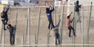 GRA079. MELILLA, 15/10/2014.- En torno a un centenar de inmigrantes permanecen encaramados en la valla fronteriza entre Melilla y Marruecos y se niegan a bajar como les indica la Guardia Civil, que mantiene un despliegue de seguridad en la zona de Villa Pilar, entre el aeropuerto de Melilla y el cementerio musulm·n de Sidi Guariach.Numerosas patrullas de la Guardia Civil han formado un cordÛn de vehÌculos a pie de valla en un tramo amplio del perÌmetro, donde los subsaharianos permanecen desde pasadas las 06:30 horas, cuando se registrÛ un intento de entrada masivo protagonizado por m·s de 200 inmigrantes. EFE/F. G. Guerrero