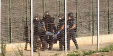 GRA016 MELILLA, 14/08/2014.- Agentes de la Guardia Civil llevan en volandas a uno de los seis inmigrantes que se encontraban en lo alto de malla antitrepa de Melilla tras un nuevo intento de entrada a la ciudad autonóma a través de la valla fronteriza con Marruecos por parte de decenas de inmigrantes subsaharianos. Tras casi dos horas encaramados a la valla los seis inmigrantes han sido obligados a descender en la zona entre vallas y entregados a la gendarmería marroquí. EFE/Francisco G.Guerrero