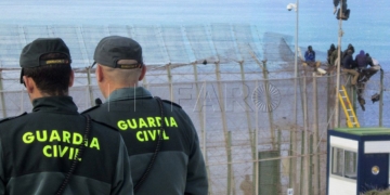 GRA295. MELILLA, 03/04/2014.- Agentes de la Guardia Civil ante los inmigrantes de origen subsahariano que permanecen en lo alto de la valla de Melilla, tras casi 10 horas encaramados a una altura de seis metros, después de protagonizar junto a otros 150 subsaharianos un intento de entrada masivo a Melilla. Dos de los inmigrantes se encuentran esta tarde en lo alto de la valla, mientras que el resto han comenzado a bajar con la ayuda de una escalera y, acompañados por agentes de la Guardia Civil. EFE/Noelia Ramos
