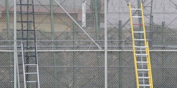 GRA009. MELILLA, 02/12/2014.- Varios subsaharianos permanecen encaramados en la valla de Melilla por la zona cercana al paso fronterizo de Barrio Chino, que está cortado al tránsito desde que a las siete de la mañana se hayan registrado dos intentos de entrada simultánea de dos grupos, con más de medio millar de inmigrantes. EFE/F. G. Guerrero