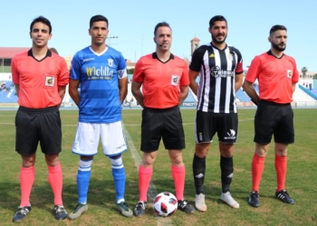 El trío arbitral, junto a los capitanes de	una y otra escuadra, destacando que el veterano melillense Mahanan volvía en la matinal de ayer al once inicial de los azulinos.