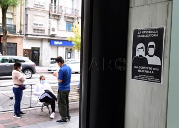 Unos vecinos conversan en la Avenida de la Albufera en el distrito del Puente de Vallecas, junto a un cartel que recuerda el uso obligatorio de mascarilla. EFE/Victor Lerena/Archivo