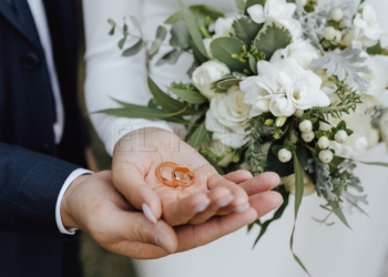 Wedding bands in the hands of bride and groom and with beautiful wedding bouquet made of greenery and white flowers