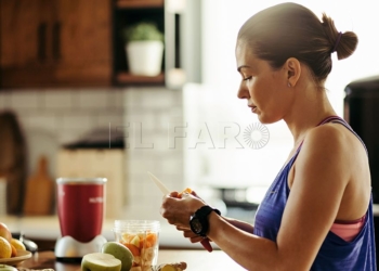 Young sportswoman making herself a healthy smoothie and slicing fresh fruit in the kitchen.