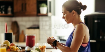 Young sportswoman making herself a healthy smoothie and slicing fresh fruit in the kitchen.