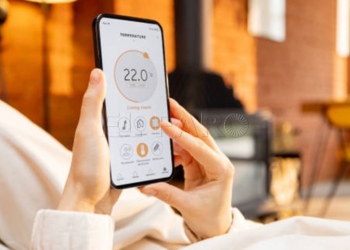 Woman holding phone with running smart home application for heating temperature control, while lying relaxed at home. Close-up on device screen