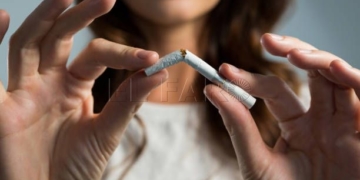 Mid section of woman breaking cigarette against white background