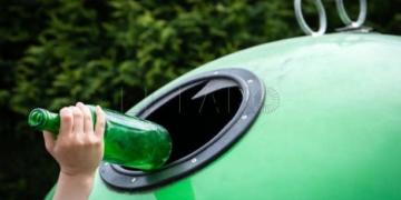 Child's hand throws the glass bottle in a green container