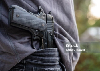 Armed man carrying a pistol in his jeans waistband, blur outdoor nature background. Threat, violence and danger concept