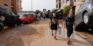 PAIPORTA (VALENCIA), 30/10/2024.- Varias personas con botellas de agua caminan entre los vehículos destrozados en la región valenciana de Paiporta a causa de las fuertes lluvias causadas por la DANA. La alcaldesa de Paiporta (Valencia), Maribel Albalat, ha confirmado que al menos hay 34 fallecidos en su municipio a consecuencia de la dana que ha afectado a la Comunidad Valenciana.  EFE/Manu Bruque