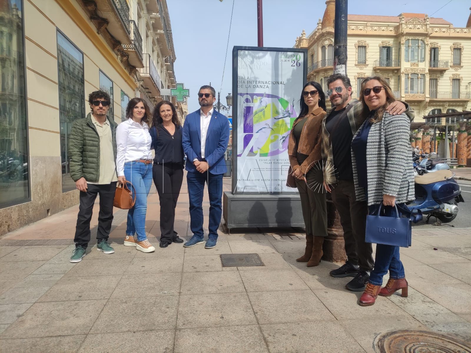Consejero de Educación, Miguel Ángel Fernández, junto a la directora de la Escuela de Música y Danza, Nuria Nieto, y profesorado del centro frente al cartel dispuesto en los mupis de Melilla. -AGC-